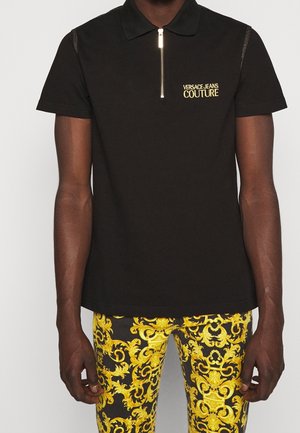 Czarna polo z krótkim rękawem z złotym logo "Versace Jeans Couture" i zamkiem błyskawicznym, zestawiona z czarnymi spodniami ozdobionymi misternymi żółtymi wzorami barokowymi.