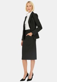 Czarna, dopasowana marynarka i ołówkowa spódnica, teksturowany materiał, biała koszula z kołnierzykiem pod spodem, zestawione z czarnymi szpilkami z długim noskiem.