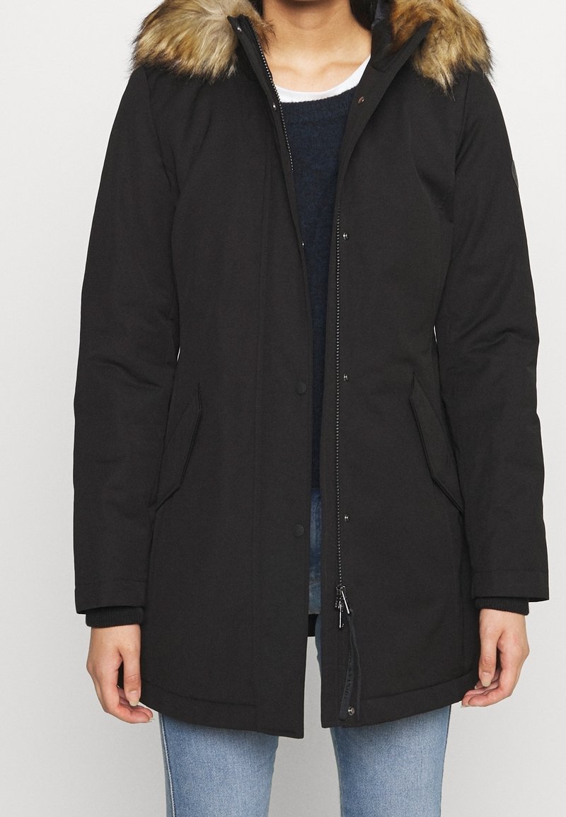 Svart parka med pälsförsedd huva, som har dragkedja och tryckknappsstängning, två sidofickor och en avslappnad passform. Tillverkad av slitstarkt, väderbeständigt material.