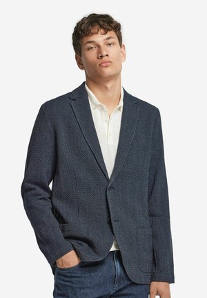 Navy blue blazer with a textured fabric, single button closure, notched lapels, and two front pockets, paired with a white polo shirt underneath.