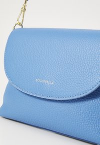 Borsa a tracolla in pelle blu con finitura testurizzata, patta arrotondata e dettaglio del logo in oro. Presenta una tracolla in metallo dorato.