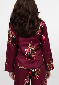 Bordeaux pyjama set met rode panda prints, met een losse pasvorm, lange mouwen en bamboe accenten. Soepele stoftextuur.