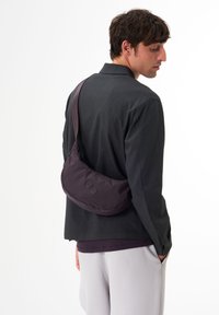 Lila Nylon-Umhängetasche mit geschwungener Form, ausgestattet mit zwei dekorativen Knöpfen und einem verstellbaren Tragegurt für vielseitige Trageoptionen.