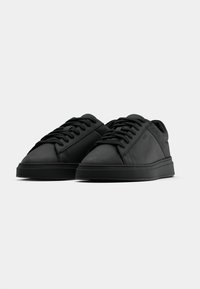 Μαύρα αθλητικά παπούτσια χαμηλού ύψους με κορδόνια, απαλό ματ φινίρισμα και διακριτικό λογότυ πο της μάρκας στο πλάι, εμφανιζόμενα πάνω σε απλό λευκό φόντο.