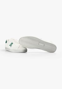 Zapatillas veganas blancas con acentos verdes, material superior liso, cierre de cordones y suela de goma texturizada con patrón de espiguilla.