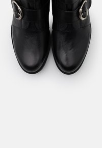 Czarne skórzane buty ankle z gładką cholewką, wąskim noskiem, podwójnymi paskami z srebrnymi klamrami i płaską gumową podeszwą.