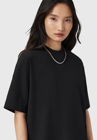 Zwart oversized t-shirt van zachte stof met een ronde halslijn en korte mouwen, gecombineerd met een zilveren en gouden ketting.
