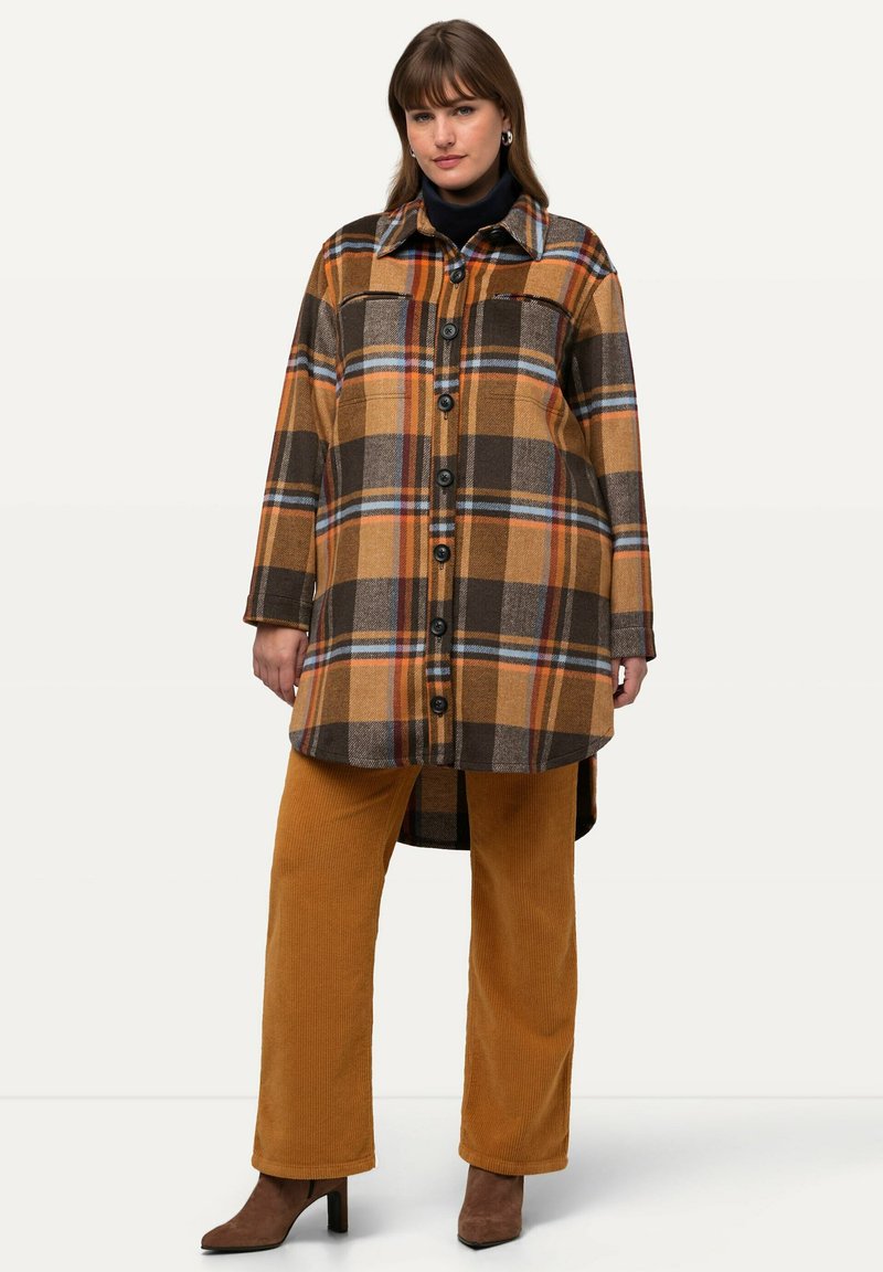 Brun och orange rutigt knappar-up kappa med krage, bröstfickor och långa ärmar, parat med senapsfärgade kordbyxor och bruna klackar.