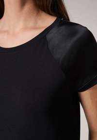 Camiseta negra de tela suave con escote redondo, mangas cortas y acentos de satén contrastantes en los hombros.