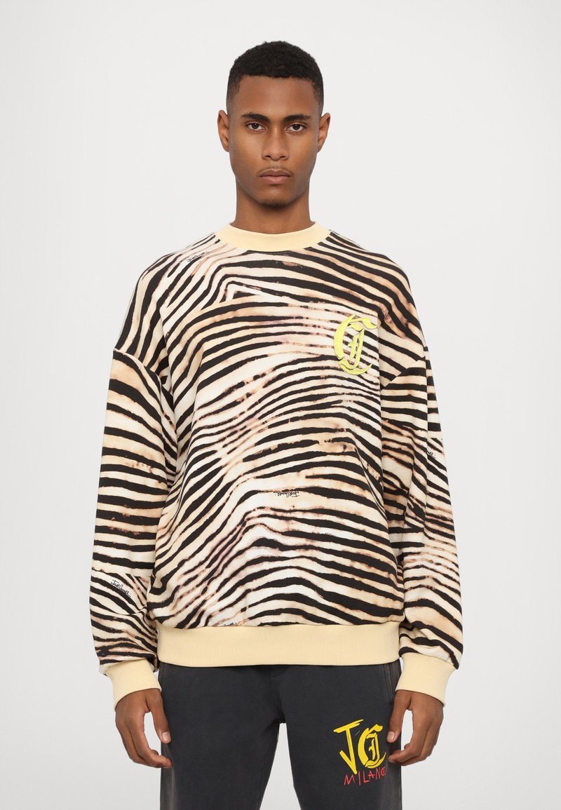 Sweatshirt med zebramönster i beige och svart, med en gul logotyp på bröstet och ribbad muddar och fåll.