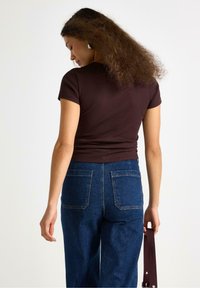 Top aderente a costine marrone abbinato a jeans di denim blu a vita alta. La parte posteriore del top presenta un collo a giro e maniche corte.