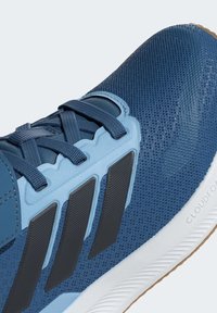 Scarpa sportiva blu scuro con tomaia in mesh traspirante, dettagli azzurri, strisce nere e suola in gomma color crema. Presenta superficie testurizzata e lacci.