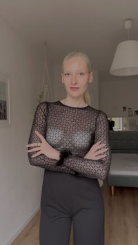 Zwart doorschijnend langarmshirt met geometrisch patroon en bontaccenten, gecombineerd met een nauwsluitende zwarte broek. Neutrale interieurachtergrond.