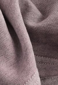Tessuto strutturato in un colore mauve tenue, caratterizzato da un motivo di maglia fine con cuciture visibili; aspetto morbido e leggermente drappeggiato.