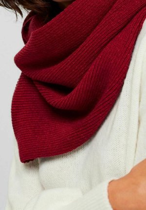 Gros plan sur une personne portant une écharpe épaisse côtelée de couleur rouge foncé par-dessus un pull en tricot blanc.