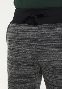 Jogging gris avec un design texturé et rayé. Caractéristiques d'une taille côtelée noire et d'un lien à nouer à l'avant. Tissu en matériau doux.