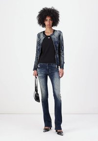 Chaqueta de denim con patrón abstracto azul, camiseta negra, jeans acampanados y bolso negro. Tacones de punta completan el atuendo.