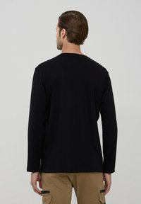 Maglia nera a maniche lunghe con scollo rotondo, realizzata in materiale morbido. Design semplice senza motivi, mostrata di schiena.