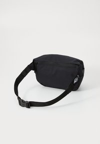 Černá látková taška se zipem, obsahující odnímatelný popruh a zaoblený tvar. Texturovaný povrch s malým logem.