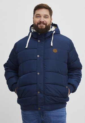 Marineblå pufferjakke med hætte, med en tekstureret quiltet design, metalknapper og et patch-logo på brystet. Casual pasform.