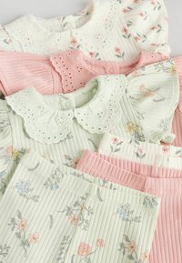 Kollektion af pastelfarvede tøj med blomsterdesigns, volangkraver og teksturerede stoffer i pink, grønne og cremede nuancer.