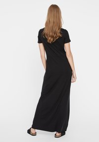 Μαύρο maxi φόρεμα από μαλακό ύφασμα, με κοντά μανίκια, σφιχτή κορυφή και μακριά, ρέουσα φούστα. Δεν αναφέρονται σχέδια ή διακοσμήσεις.