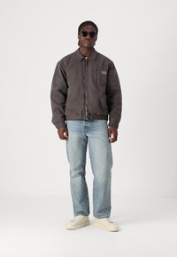 Pelēks, ar rāvējslēdzēju aizvērs bomber jakas modelis ar krūšu kabatu, vilkta virs gaiši zilām džinsām un baltām kedām. Modelis arī nēsā tumšas saulesbrilles.