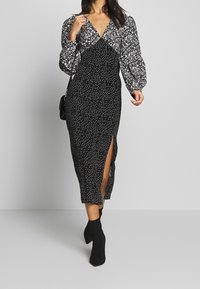 Vestido midi de estampado floral en blanco y negro con mangas largas tipo globo, escote en V y abertura lateral. Combinado con botas negras de tobillo.