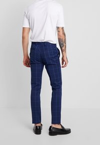 Mörkblå rutiga byxor med slim fit-design, med en slät tygtextur och bakfickor, samt ett enfärgat vitt t-shirt.