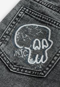 Poche en denim gris avec un graphisme de crâne stylisé peint en blanc et gris foncé avec des détails usés.