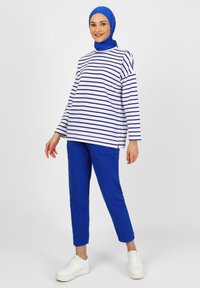 Maglietta a maniche lunghe a righe in bianco e blu navy, abbinata a pantaloni blu brillante. Completata con sneakers bianche e un hijab blu abbinato.
