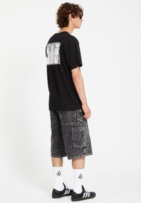 Black cotton t-shirt with graphic print on the back, paired with dark grey cargo shorts featuring multiple pockets and a faded texture.