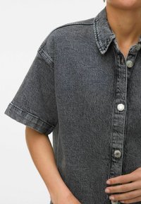 Camicia oversize a maniche corte in denim nero lavato, con patta di bottoni, tessuto testurizzato e risvolti sui polsini.