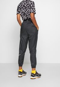 Svarta sportiga joggerbyxor med elastiska mudd och fickor. Matchade med svarta, gula och flerfärgade sneakers. T-shirt med giraffmönster synlig.