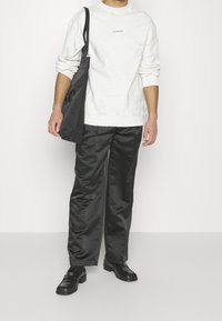 Bílá mikina s kulatým výstřihem, spárovaná s černými saténovými kalhotami a černými šněrovacími botami. Obsahuje tašku přes rameno.