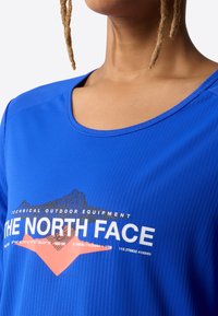 Modrá technická venkovní košile s kulatým výstřihem, texturovanou látkou a grafickým potiskem s nápisem "The North Face" a motivem hory.