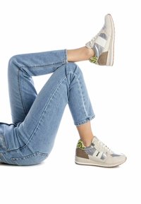 Zapatillas que combinan materiales en tonos gris y beige, con acentos metálicos y un talón texturizado en verde y beige. Combinadas con unos jeans de color azul claro.