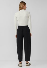 Biały bluzka z długim rękawem w cętki, zestawiona z czarnymi, wysokonasadowanymi spodniami o luźnym kroju i dwoma tylnymi kieszeniami, uzupełniona swobodnymi trampkami.