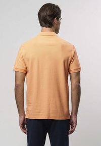 Lühikeste varrukatega polo särk heledas oranžis kangas, klassikalise krae, õmbleeritud õlaplaatide ja külgedel lõhikuga sirge äärisega.