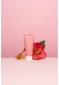 Hibiskus fuktgivande hårbottenpaket i en rosa tub, blommönster på etiketten, placerad bredvid en honungsdipper och en stor hibiskusblomma.