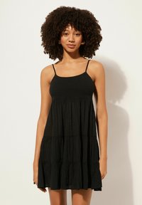 Schwarzes ärmelloses Kleid mit einem gerafften Oberteil, gestuftem Rock und fließender Textur. Dünne Träger und eine lockere Passform runden das Design ab.