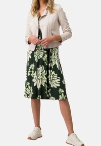 Beige motorcykeljakke i kunstlæder med lynlåslommer og en grøn blomsterkjole med store hvide og grønne blomster. Casual hvide sneakers.