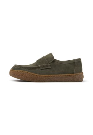 Olivengrøn ruskind slip-on sko med en tyk, tekstureret brun sål og en syet rem tværs over toppen, vist fra siden på en hvid baggrund.