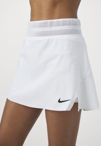 Falda de tenis blanca con una cinturilla de malla transpirable, un diseño elegante y un logo negro de Nike en la parte inferior izquierda.