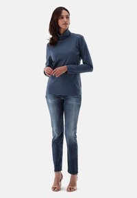 Langärmliges, Rollkragenoberteil aus dunkelblauem Stoff, kombiniert mit hellblauen, verwaschenen Jeans und beigen High-Heels.