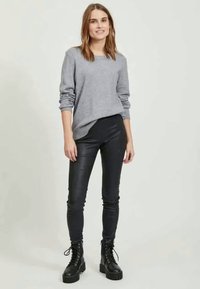 Sivi pleteni pulover z rebrastim robom v kombinaciji z črnimi usnjenimi skinny hlačami. Model nosi masivne črne čipkaste čevlje. Minimalističen dizajn.