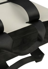 Sac en nylon noir avec des poignées solides, une ouverture zippée et un intérieur gris lisse. Présente une forme rectangulaire et un design minimal.