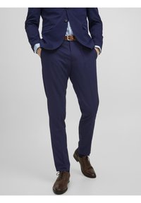 Námořnický oblek na míru s elegantním designem, hladkým materiálem a rovnými kalhotami. Hnědé kožené boty s kulatou špičkou a šněrováním.