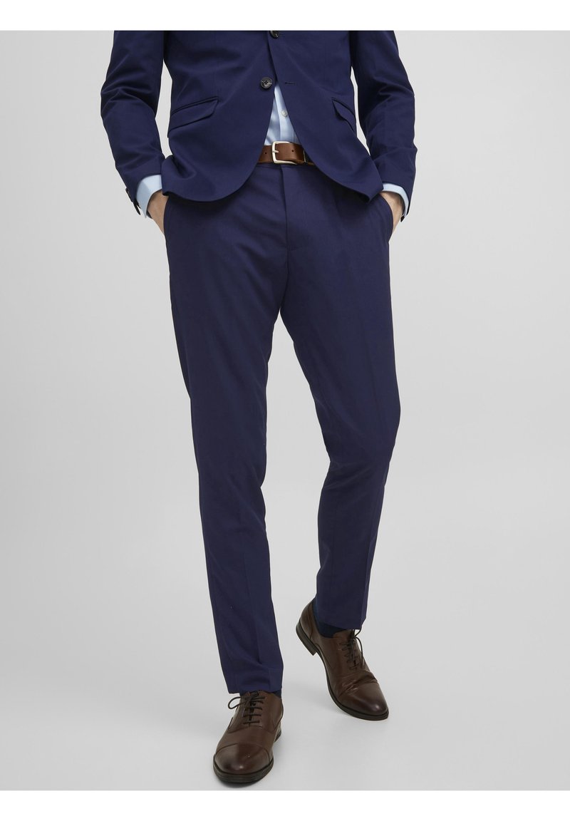 Námořnický oblek na míru s elegantním designem, hladkým materiálem a rovnými kalhotami. Hnědé kožené boty s kulatou špičkou a šněrováním.