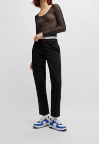 Pantalons noirs ajustés avec une texture lisse, associés à un haut long à manches transparentes noir. Mettant en valeur un accent bleu au niveau de la taille. Baskets blanches et bleues.